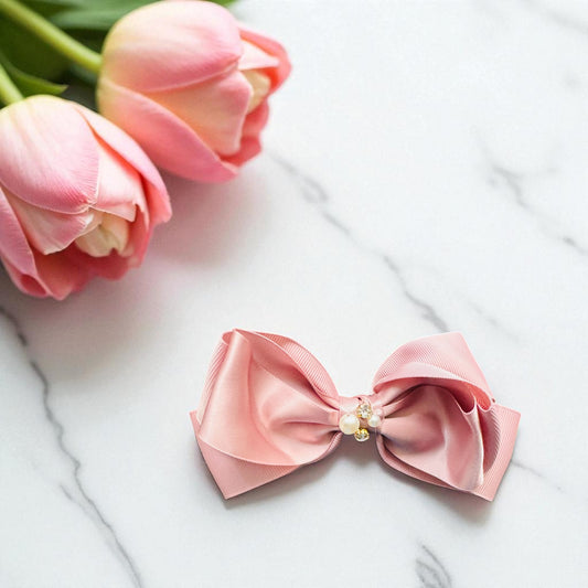 Pink bow hair clip with a pearl on a marble surface with pink tulips.
