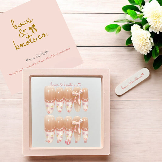Press-on nails set with packaging and floral decoration on a wooden surface