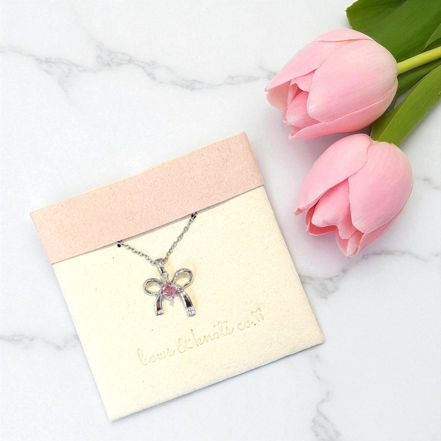 Butterfly necklace on a card with pink tulips on a marble background