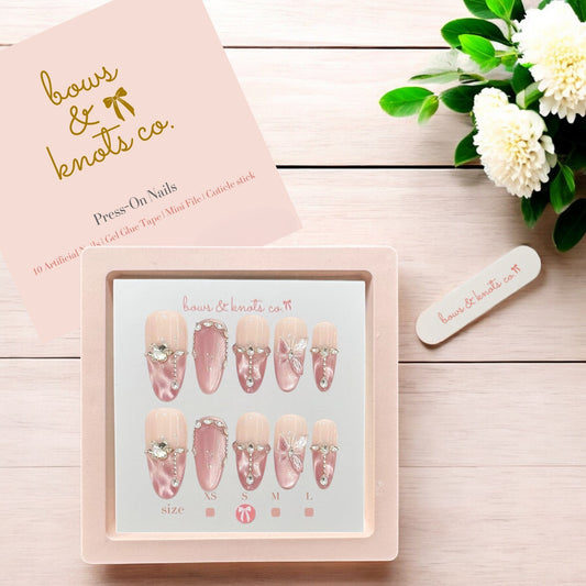 Press-on nails set with a pink box on a wooden surface, featuring the brand 'bows & knots co'.