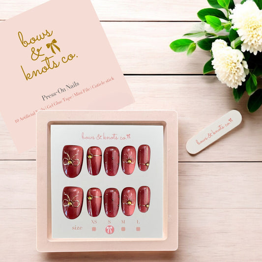 Set of press-on nails with a pink box labeled 'bows & knots co.' on a wooden surface with flowers.