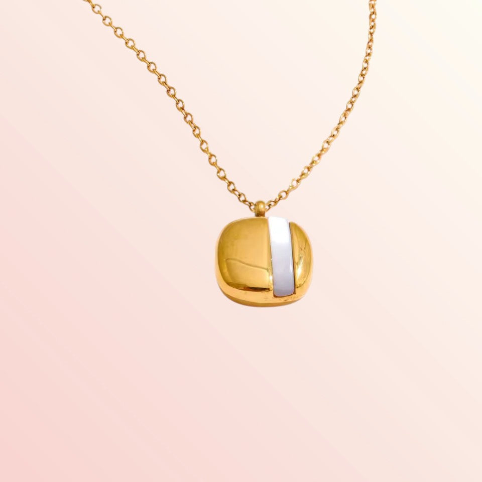Gold necklace with a square pendant on a light pink background