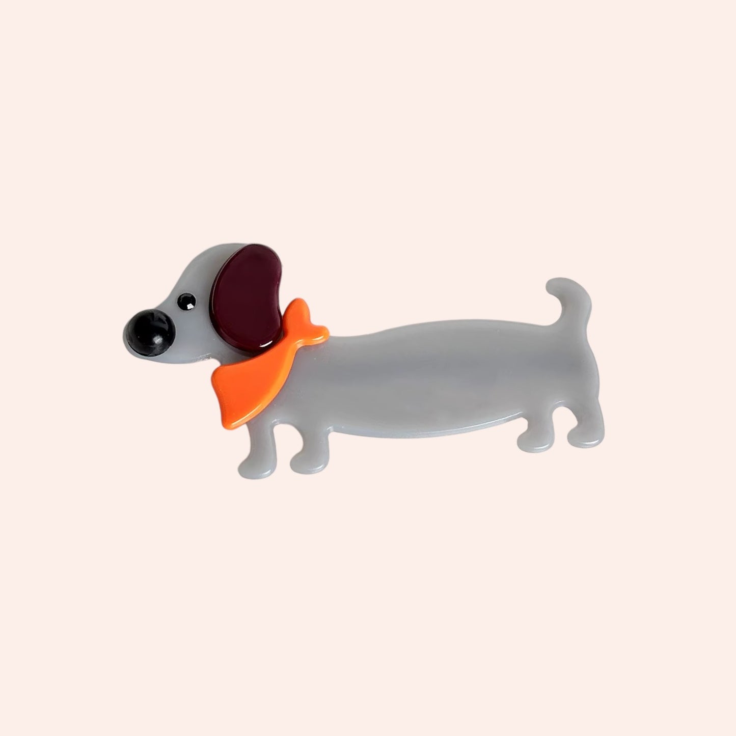Dog-shaped hair clip with a red bow tie on a beige background
