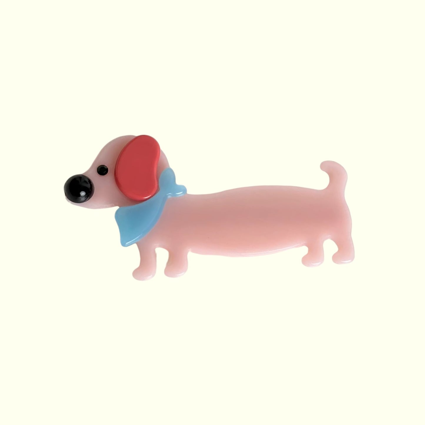 Pink dog shape hair clip with a red bow on a white background