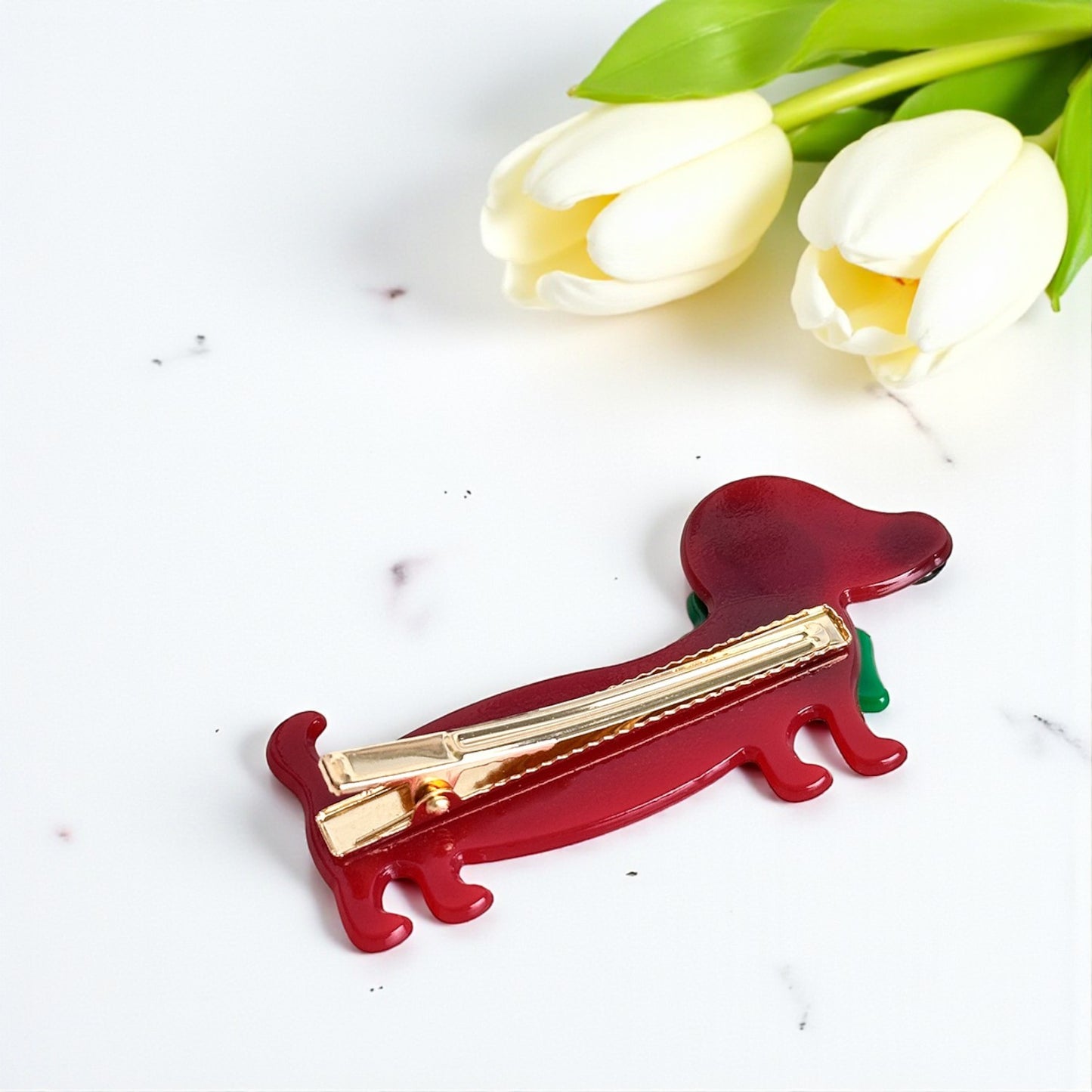 Red dog-shaped hair clip with gold barrette on a white background with white tulips.
