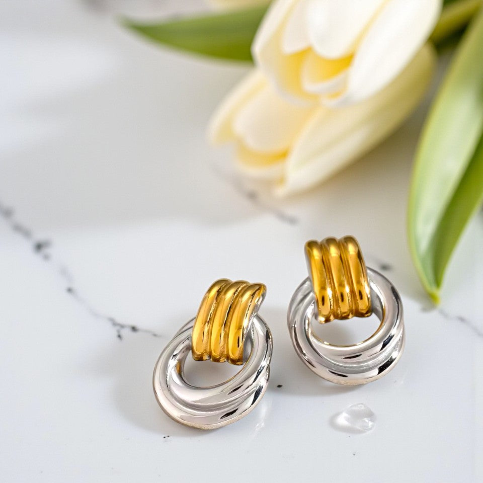 Gold and silver earrings on a marble surface with tulips in the background
