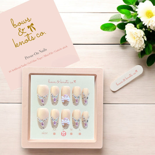 Set of press-on nails with decorative designs, packaging, and flowers on a wooden surface.