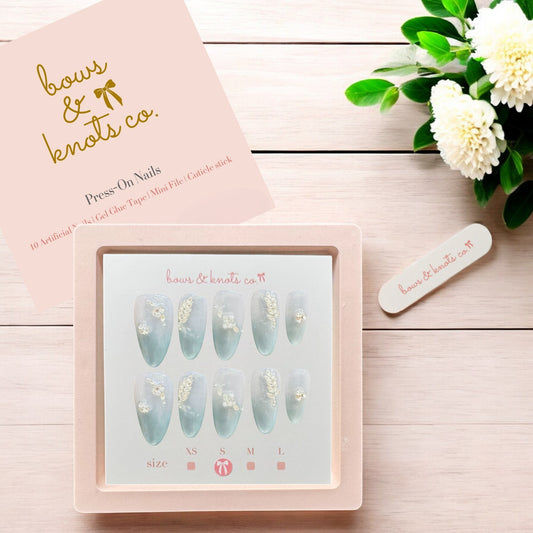 Press-on nails set with packaging and floral decoration on a wooden surface