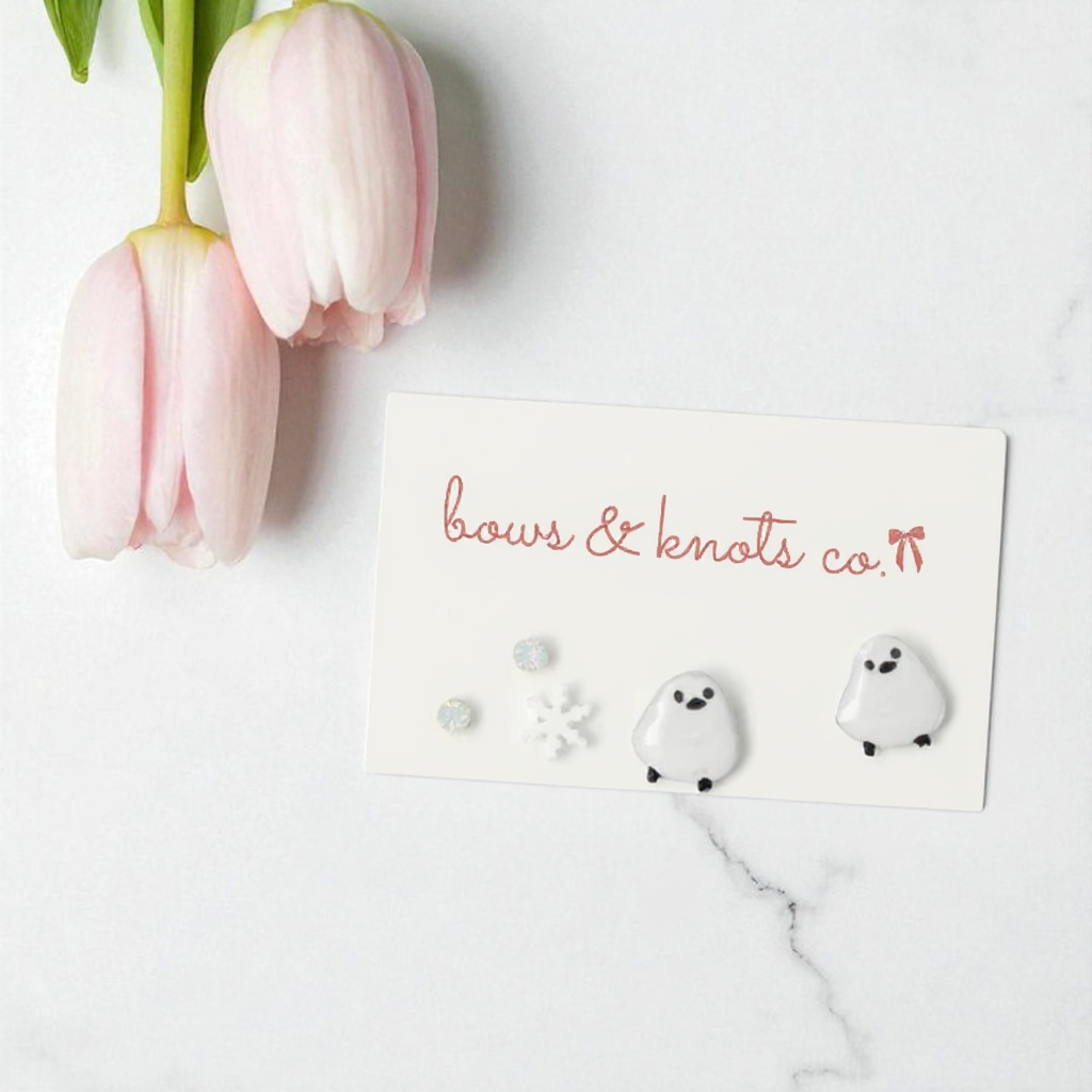 Ghost-shaped earrings on a card with pink tulips on a white marble surface