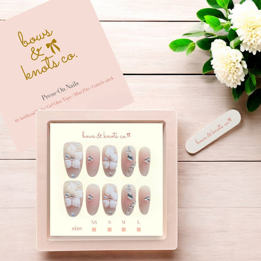 Set of press-on nails with a display card and floral decoration on a wooden surface.