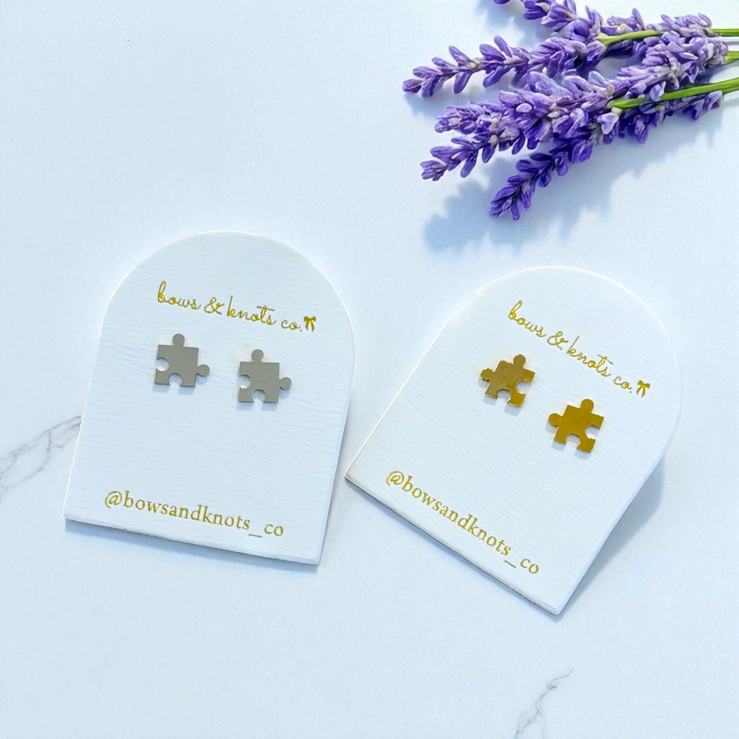 Silver puzzle piece earrings on branded card with lavender flowers on light blue background
