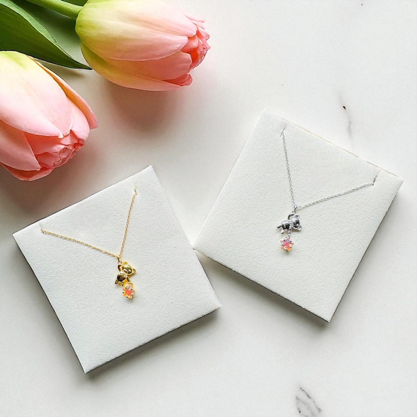 Two necklaces in display cases with pink tulips on a white surface