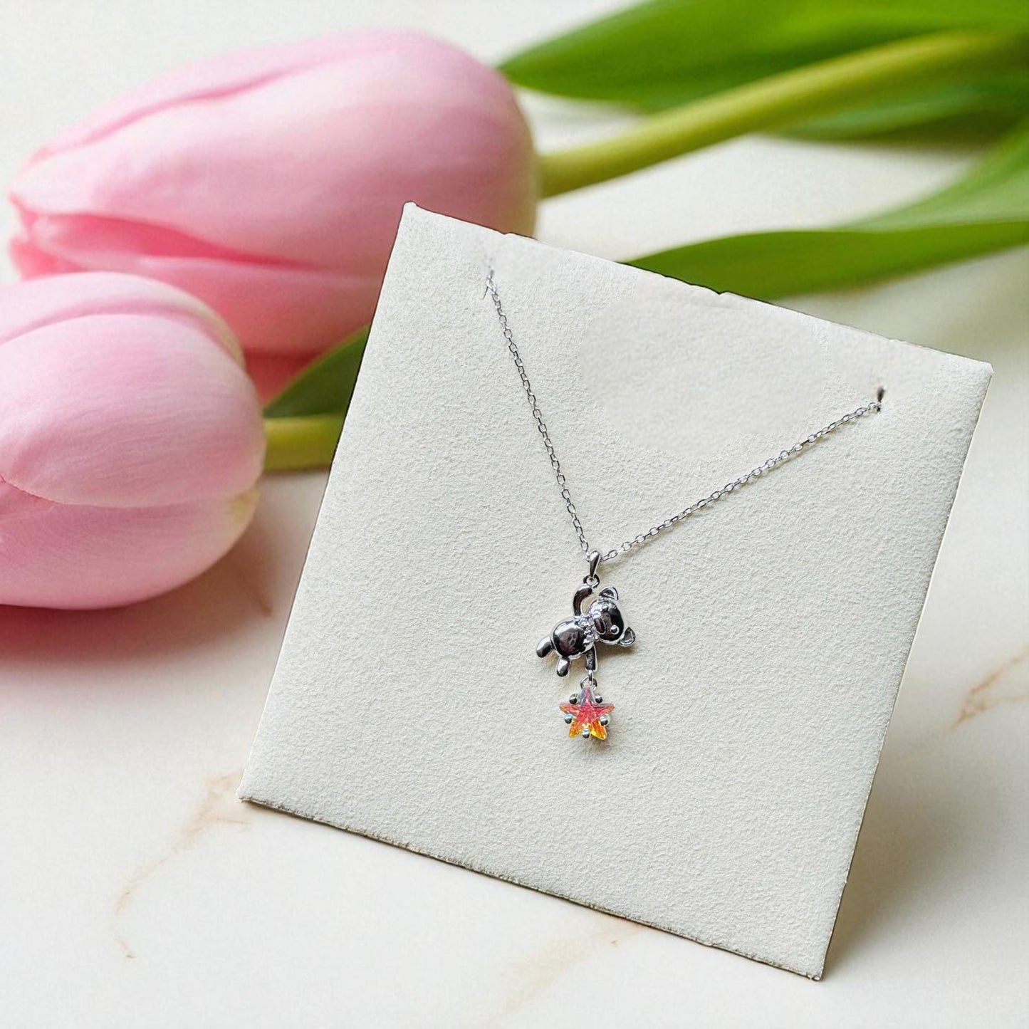Necklace with a cat-shaped pendant on a white card with pink tulips in the background