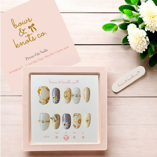 Bows & Knots Co. press-on nails set on a wooden surface with a pink box and flowers.
