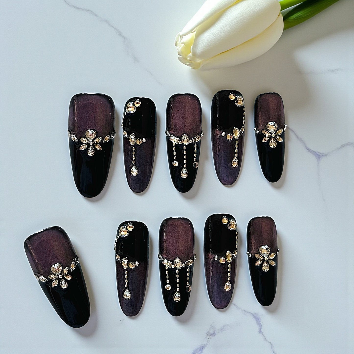 Black nail art designs with decorative elements on a marble surface with white tulips.