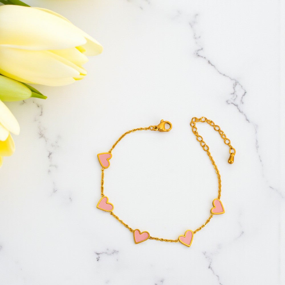 Gold bracelet with pink heart charms on a marble surface with yellow tulips.