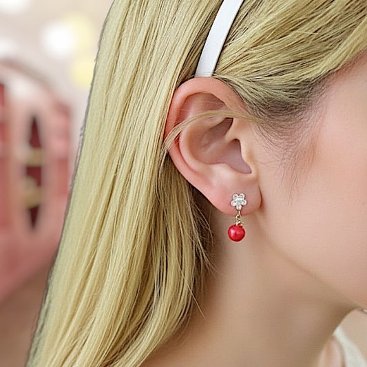 Close-up of a person wearing a red earring with a clear gemstone.