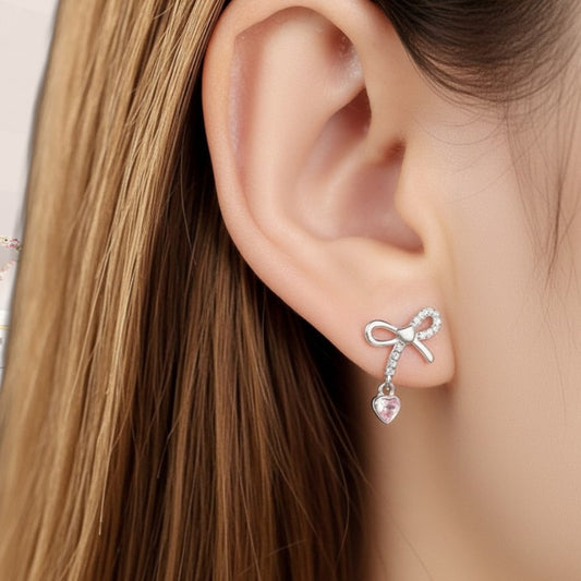 Silver bow-shaped earring with a heart detail worn by a person with long brown hair.
