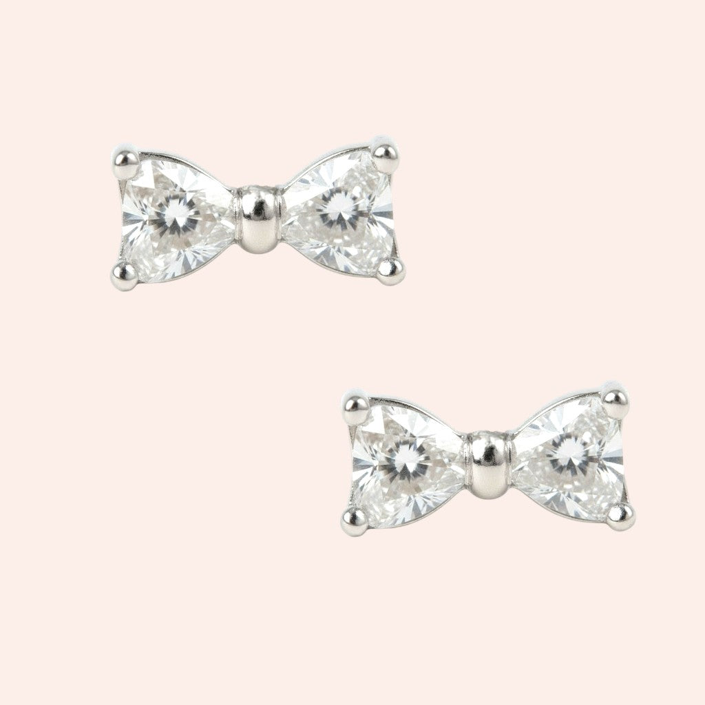 Bow-shaped earrings with clear gemstones on a light pink background