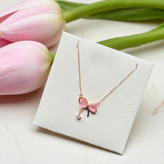 Necklace with a pink butterfly pendant on a white card, surrounded by pink tulips.
