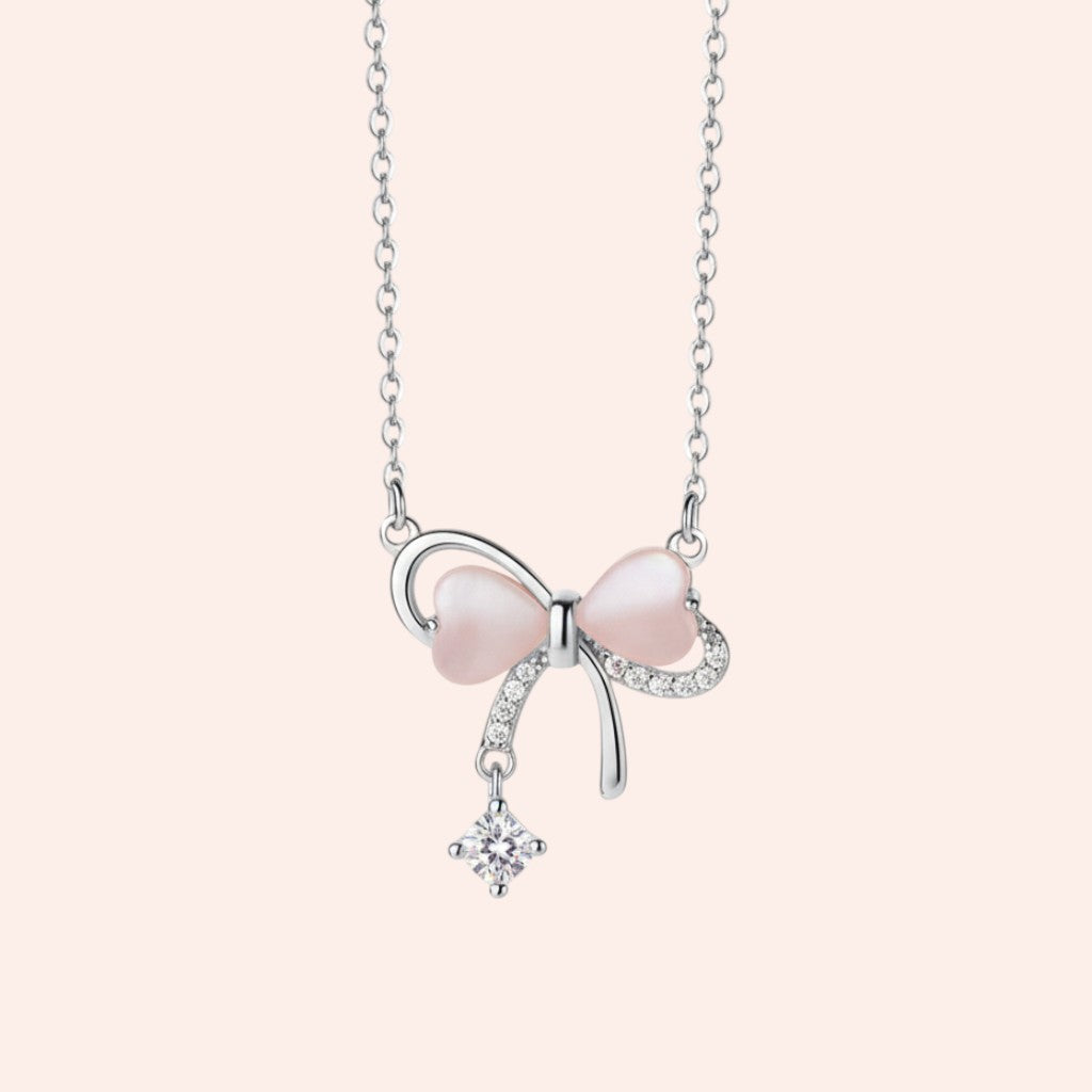 Necklace with a pink bow pendant and small diamond on a light pink background