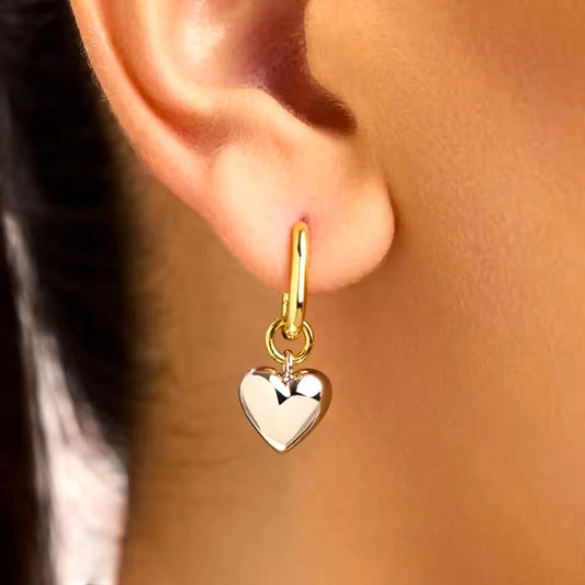 Gold heart-shaped earring worn on an ear with a blurred background