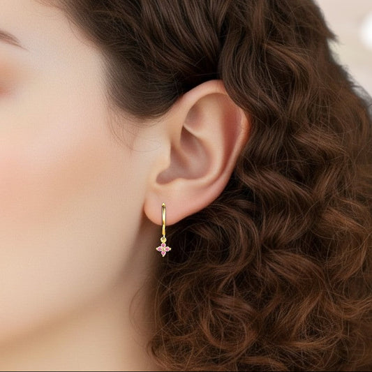 Close-up of an ear wearing a gold earring with a pink gemstone, against a blurred background.