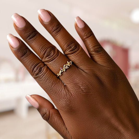 Hand wearing a gold ring with pink gemstones against a blurred background