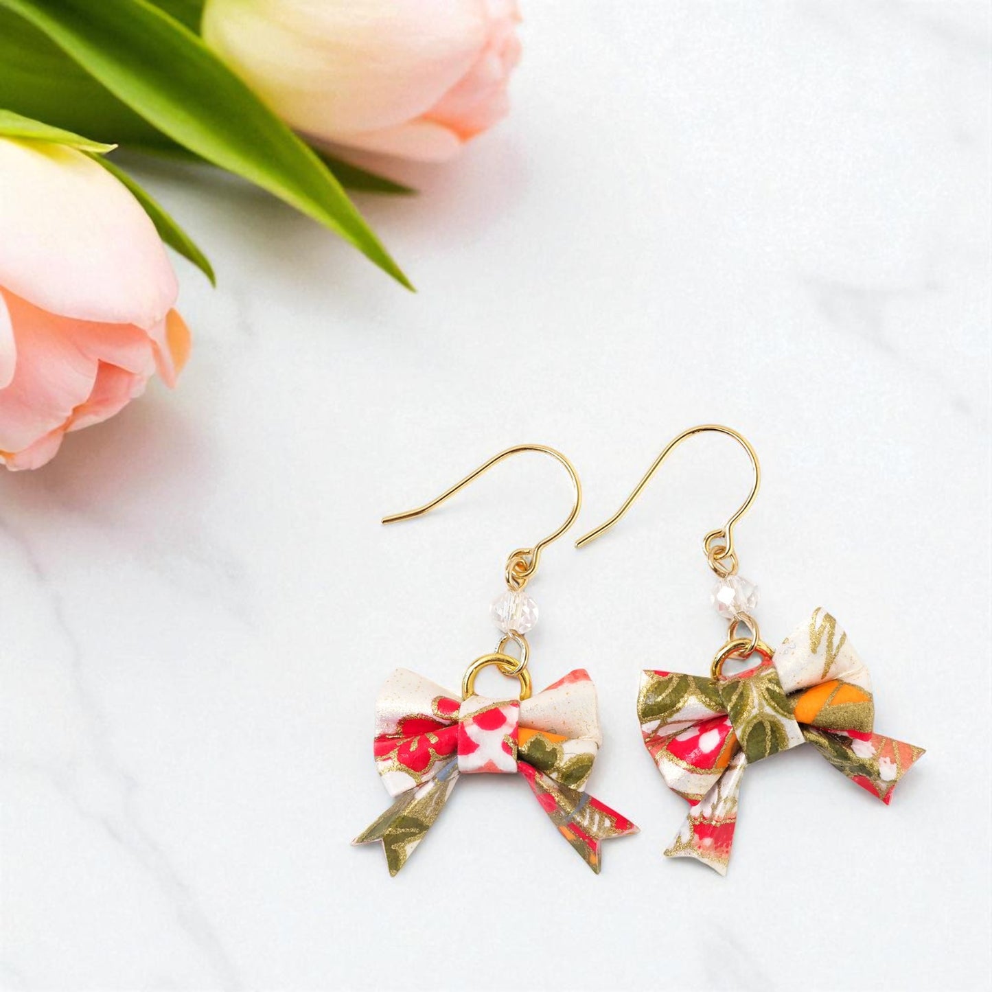 Floral bow earrings on a white surface with pink flowers and green leaves.