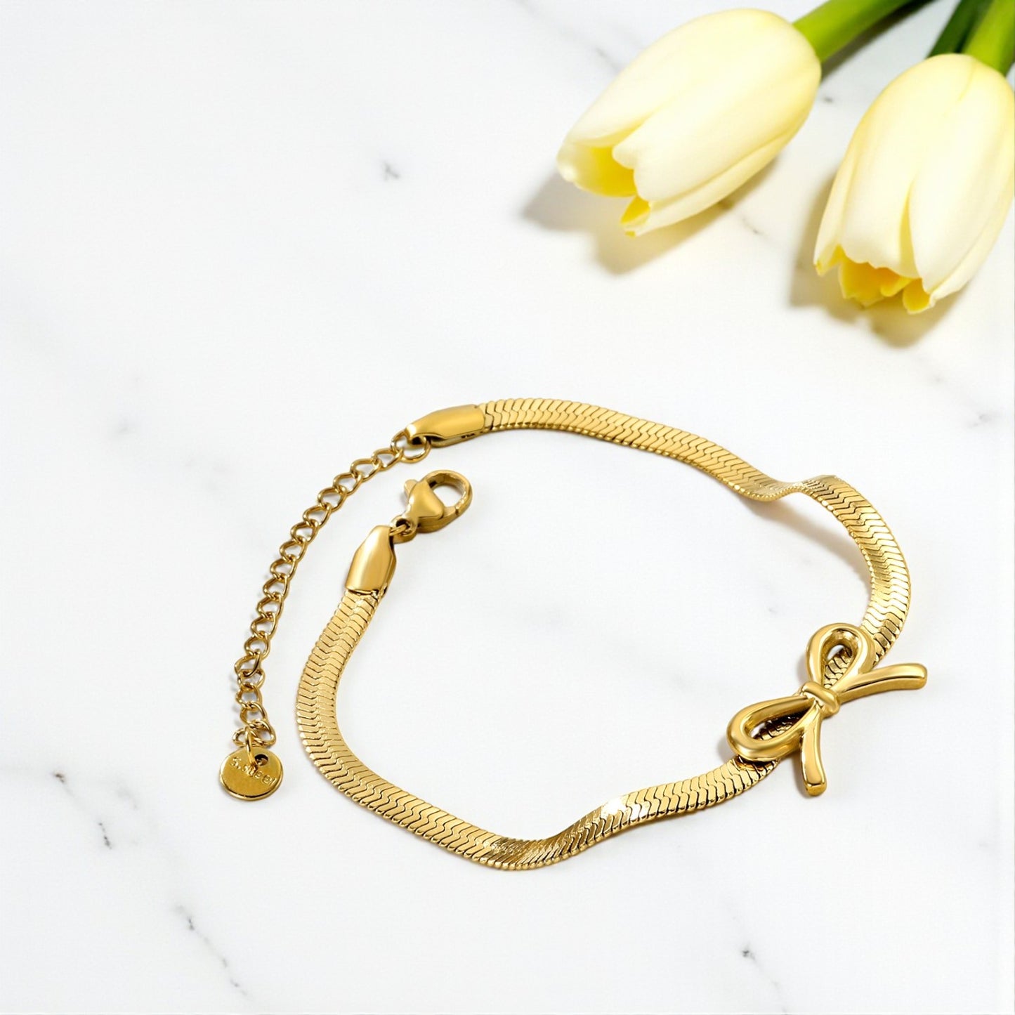 Gold bracelet with bow charm on a white surface with yellow tulips.