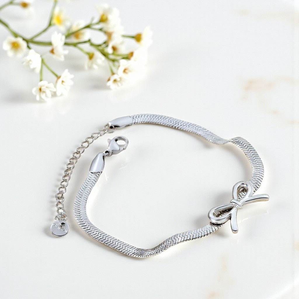 Silver bracelet with a bow charm on a light background with flowers