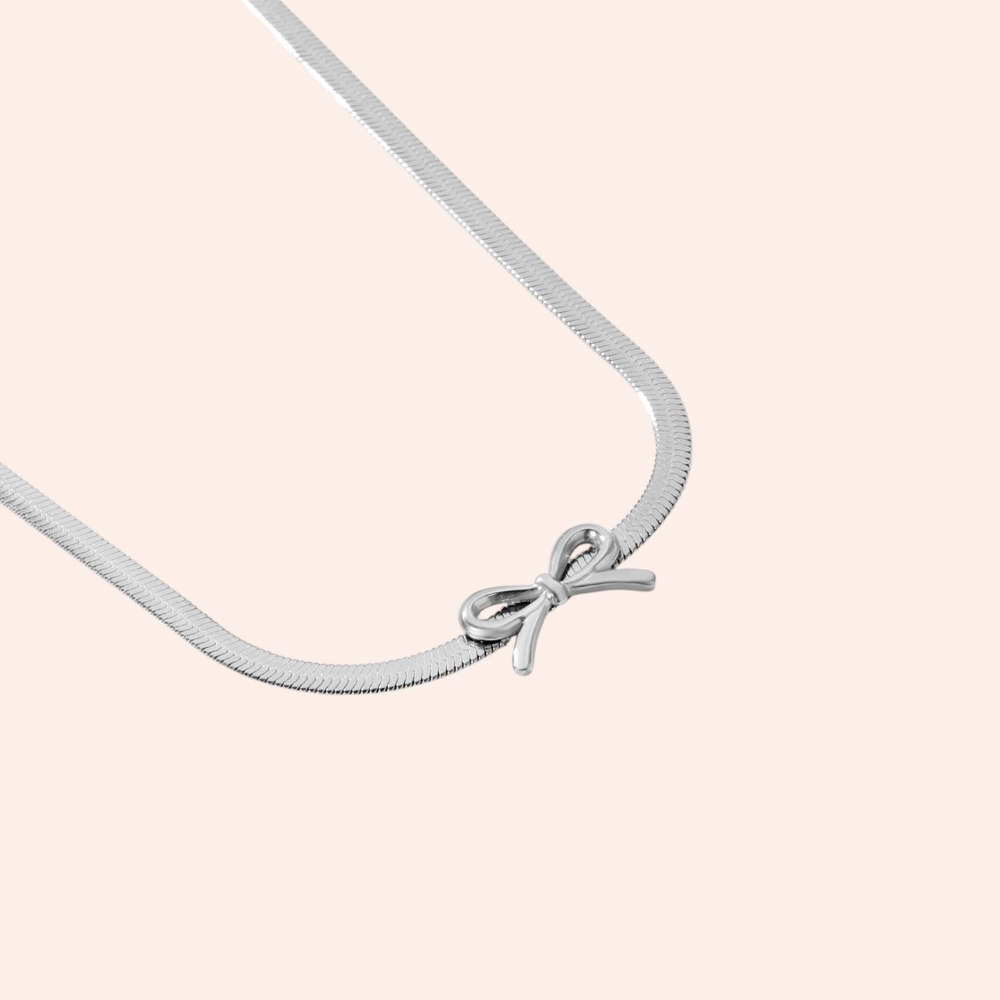 Silver necklace with a bow pendant on a light pink background