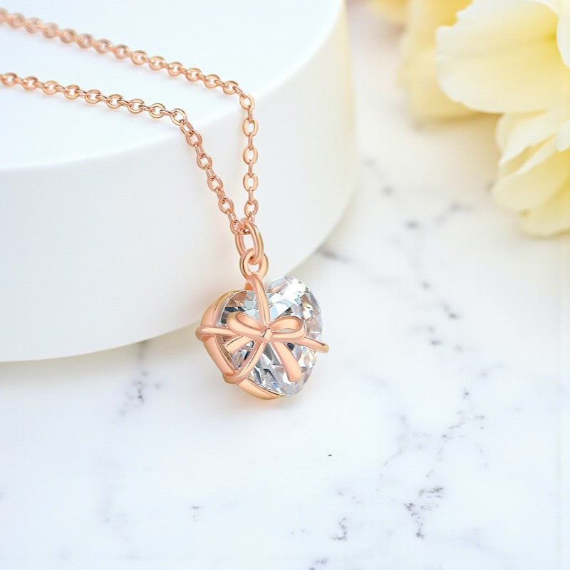 Rose gold necklace with a heart-shaped pendant on a marble surface with a yellow flower.