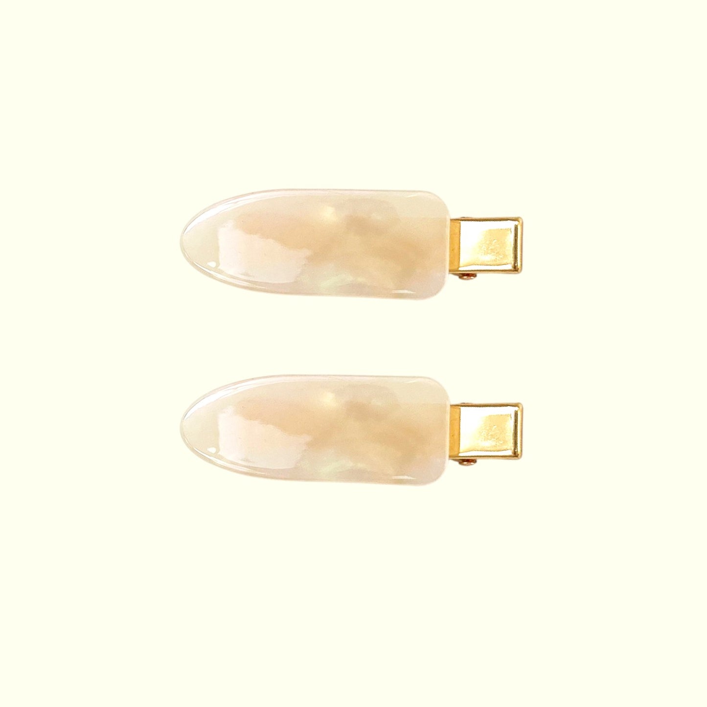 Two beige nail extensions with gold clips on a white background