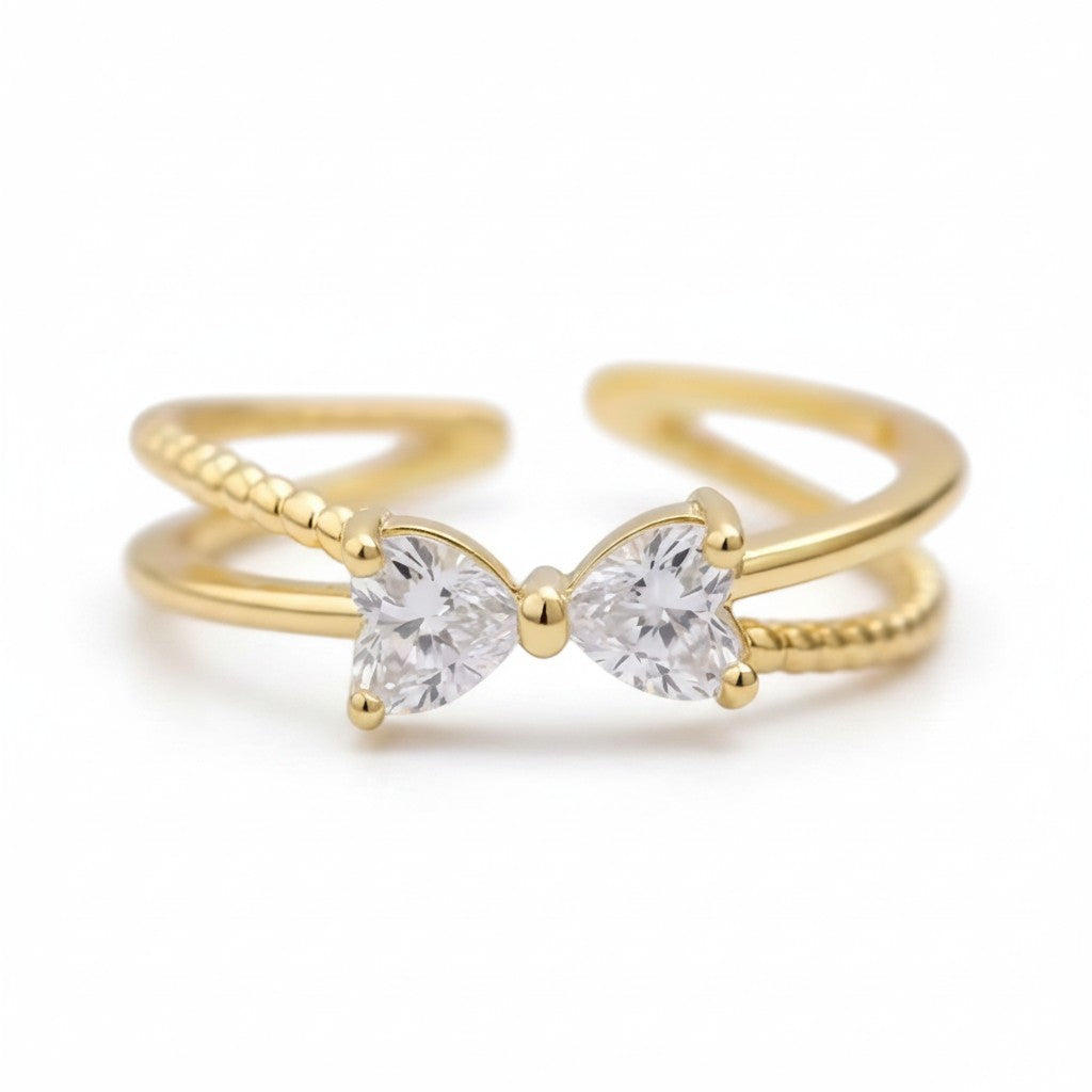 A gold adjustable ring featuring a bow-shaped setting with two clear pear-cut gemstones, photographed on a clean white background.