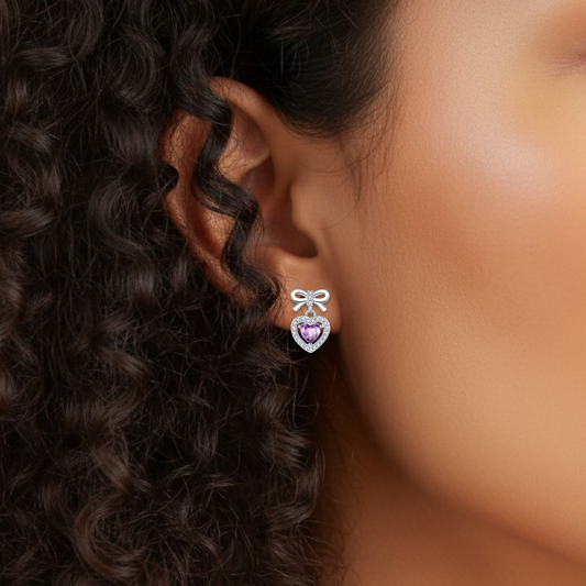 Close-up of an ear wearing a heart-shaped earring with a purple gemstone.