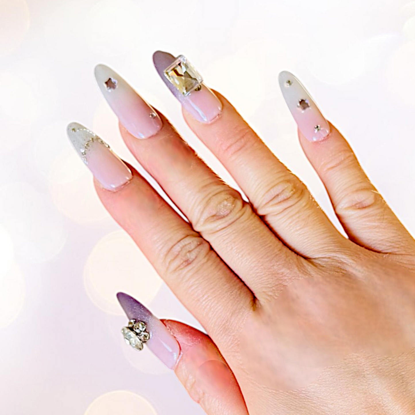 Hand with pink and white gradient nails featuring rhinestones on a white background