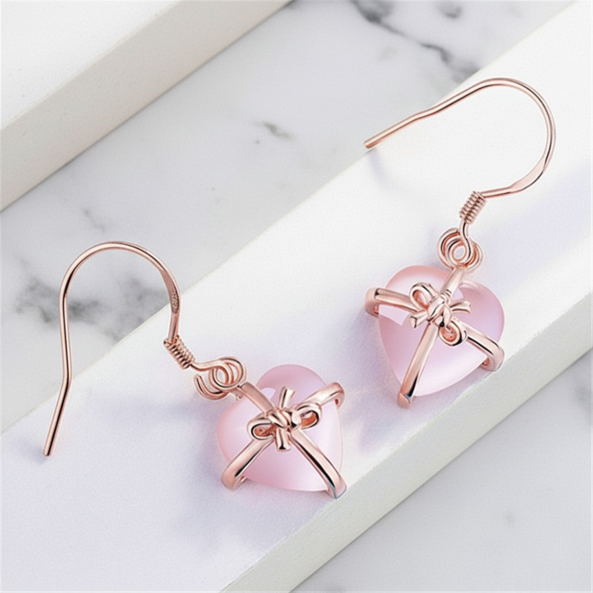 Heart-shaped earrings with pink hearts and rose gold bows on a marble surface