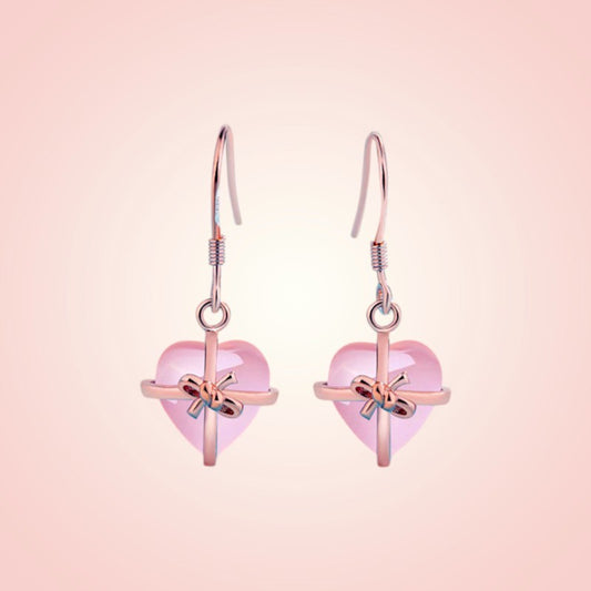 Heart-shaped earrings with pink hearts and gold bows on a pink background