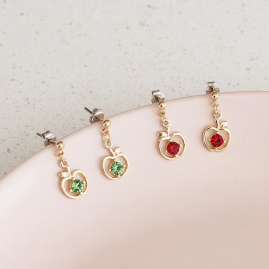 Gold heart-shaped earrings with green and red gemstones on a light background