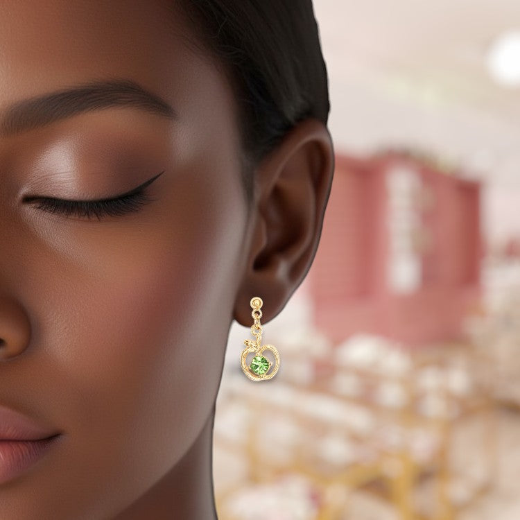Close-up of a woman wearing gold earrings with green gemstones, blurred background