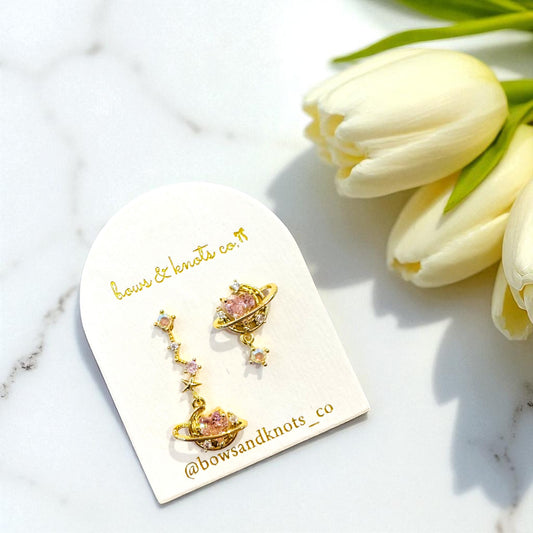 Gold earring with pink stones on a branded card next to white tulips