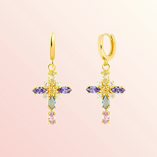 Gold cross-shaped earrings with colorful gemstones on a pink background