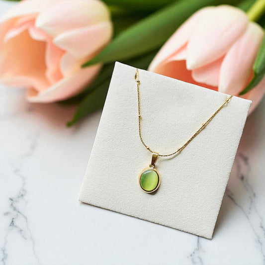 Gold necklace with a green pendant on a white card, with pink tulips in the background.