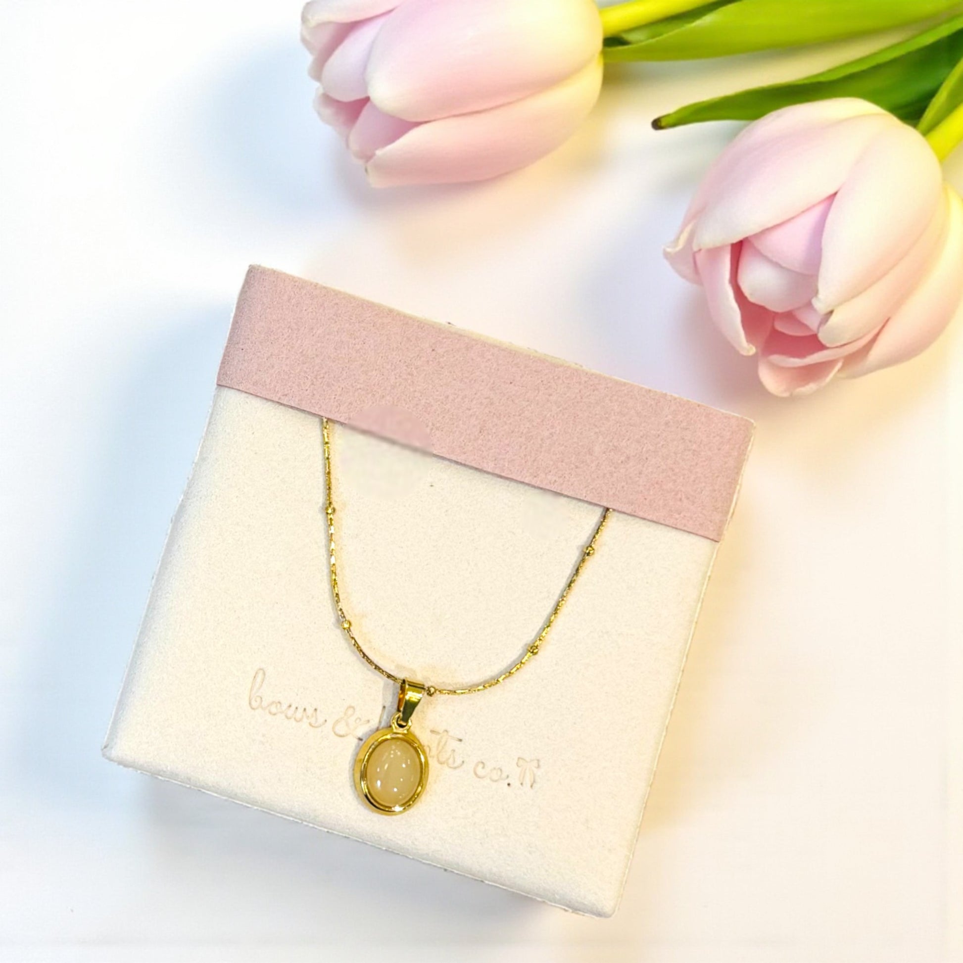 Gold necklace on a pink jewelry box with tulips in the background
