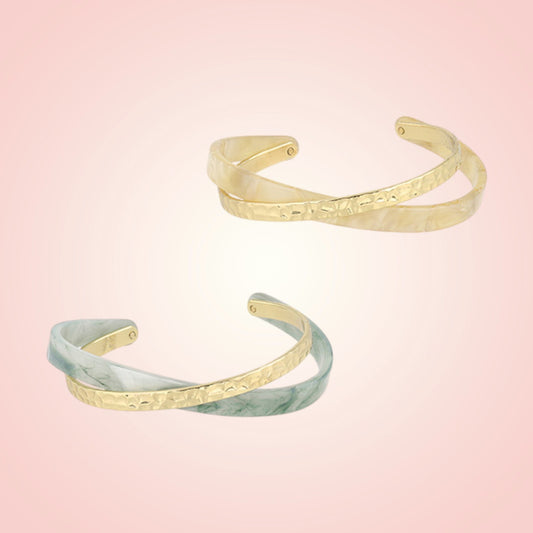 Two gold and green marble patterned cuffs on a gradient pink background