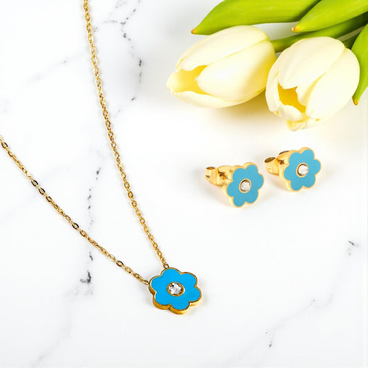 Jewelry set with blue flower-shaped pendants on a marble surface with tulips.