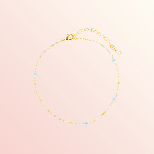 Gold bracelet with small blue stones on a light pink background