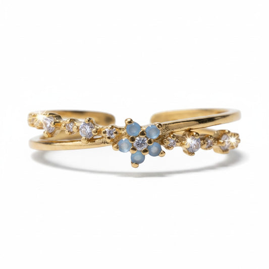 A gold double-band ring featuring a central cluster of light blue round stones and small clear stones, photographed on a clean white background.