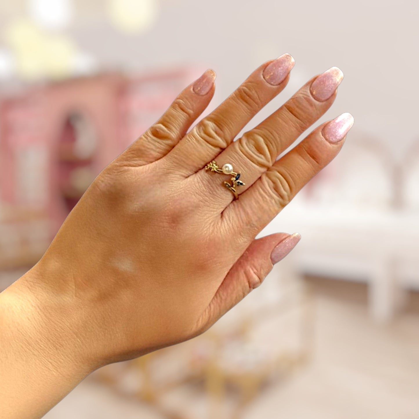 Hand wearing a gold ring with a pearl on a blurred background